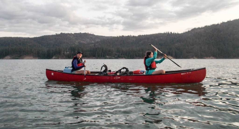 two girls paddle a red canoe on still water